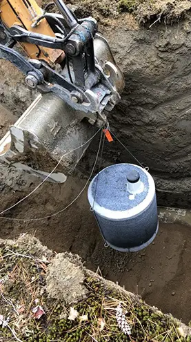 Construction equipment from groupe h2o installs a surface well in an excavation, with a cylindrical reservoir positioned to be buried underground.