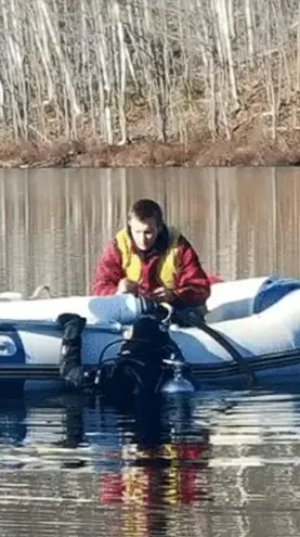 A technician from groupe h2o in a safety vest is on an inflatable boat in the middle of a lake, installing a water intake system. The forest is visible in the background.